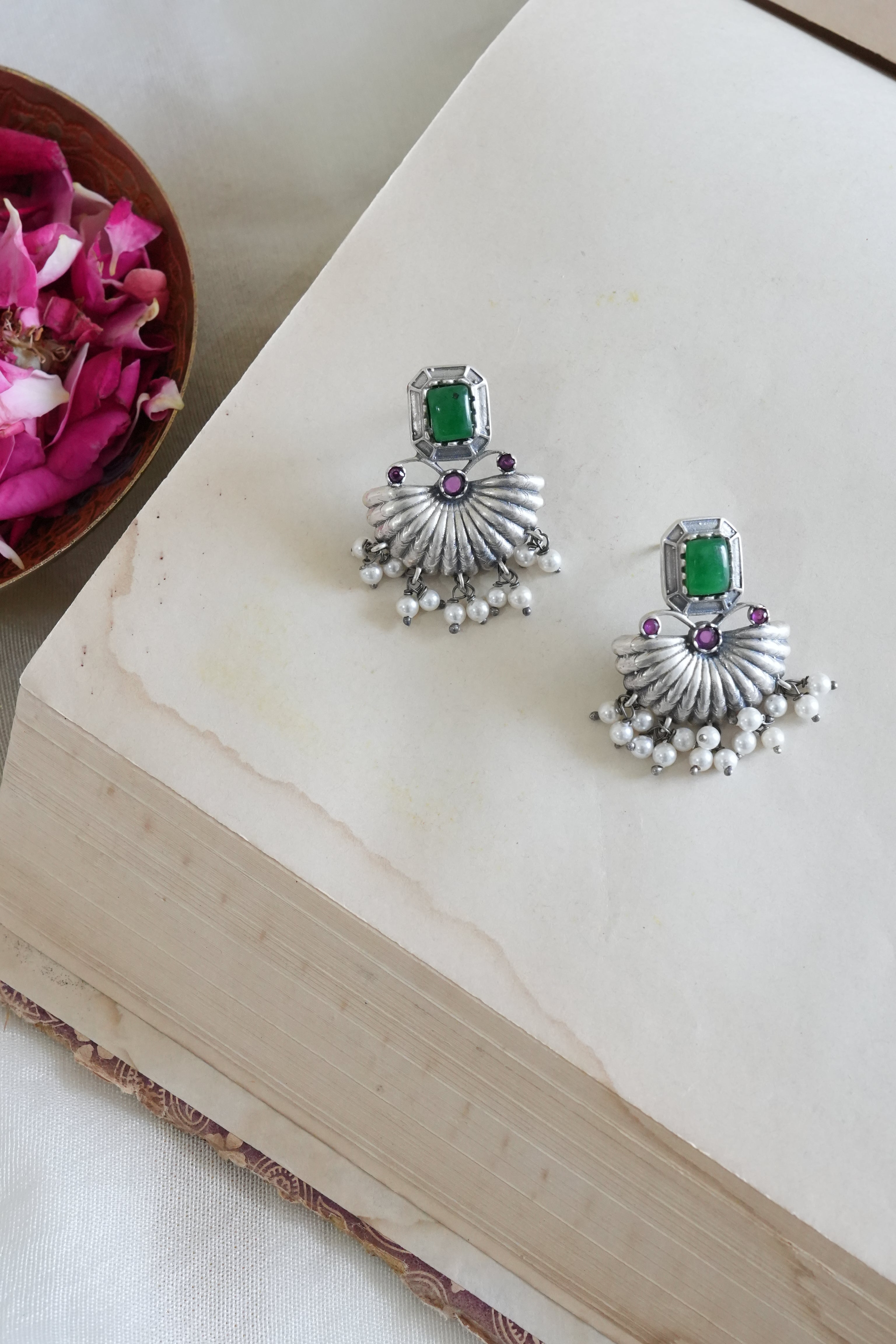 Silver earrings with green and purple stones on a white surface